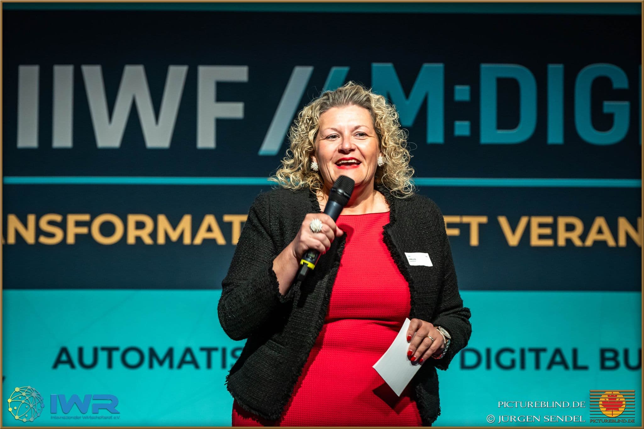 Sprecherin mit Mikrofon vor dem Bühnenbild „IIWF // M:DIGITAL“.